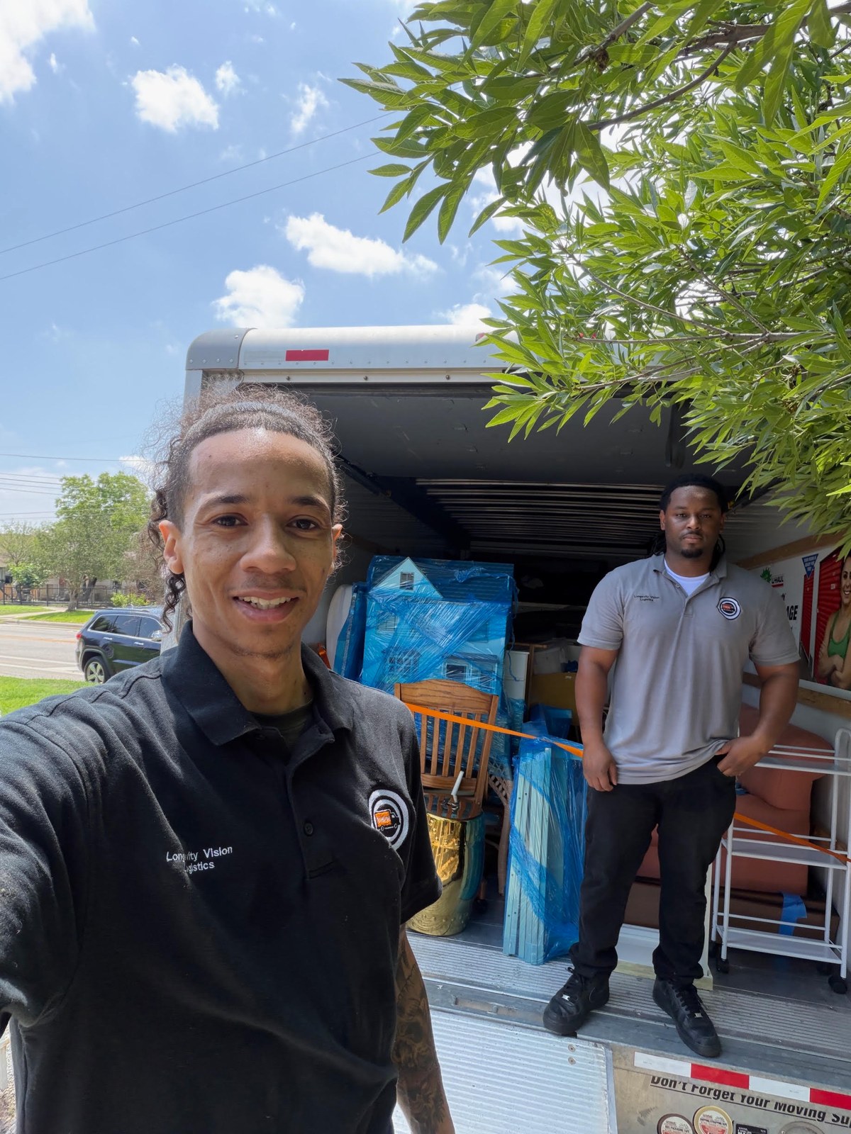 Two Longevity Vision team members beside their moving truck, with furniture protected for the move